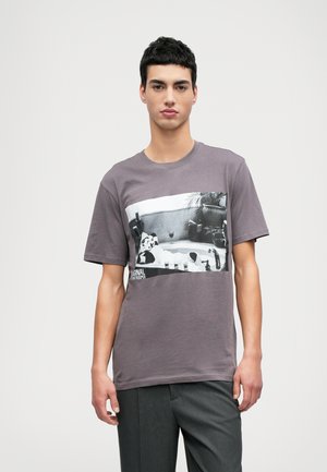 Grå bomulds T-shirt med et sort og hvidt grafisk print på brystet. Korte ærmer og rund halsudskæring.