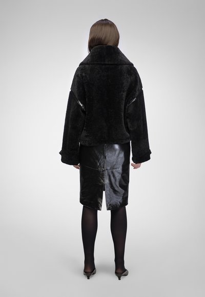 Zwarte nep bontjas met een uitgesproken kraag en een loose fit, gecombineerd met een glanzende zwarte kokerrok met een diepe split aan de achterkant.