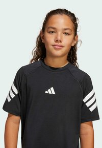 Črna kratkotrajna atletska majica s kratkimi rokavi, ki ima bele tri črte na rokavih in bele logotip na prsih. Gladka tekstura blaga.