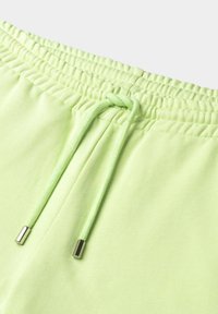 Pantalones cortos de algodón verde claro con una cinturilla elástica y cordón que presenta detalles de ojales metálicos. Textura suave con acentos acanalados.
