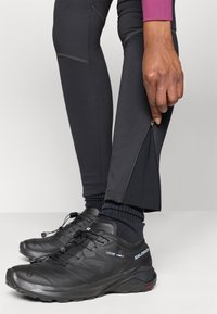 Zwarte sportleggings met zijritsen, gecombineerd met zwarte wandelschoenen met een gestructureerd oppervlak en elastische veters.