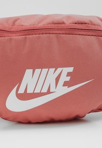 Röd tygpåse med en strukturerad yta, med en framträdande vit Nike-logotyp och en dragkedjestängning upptill.