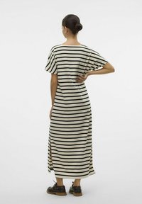 Robe maxi rayée en crème avec des rayures noires, à manches courtes amples, avec des fentes sur les côtés et une coupe décontractée. Modèle portant des chaussures foncées.