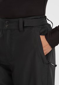 Zwarte broek van gladde stof, met een verstelbare tailleband met knopen, zijzakken en subtiele logo-details op de rand.