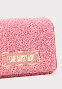 Portafoglio rosa sfumato con superficie morbida e texture, dotato di una placca dorata con la scritta "LOVE MOSCHINO". Bordo curvo con dettagli cuciti.