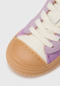 Baskets violettes et crème avec une tige en daim texturé, un embout en caoutchouc et une semelle beige. Dotées de lacets blancs épais et de détails de coutures.
