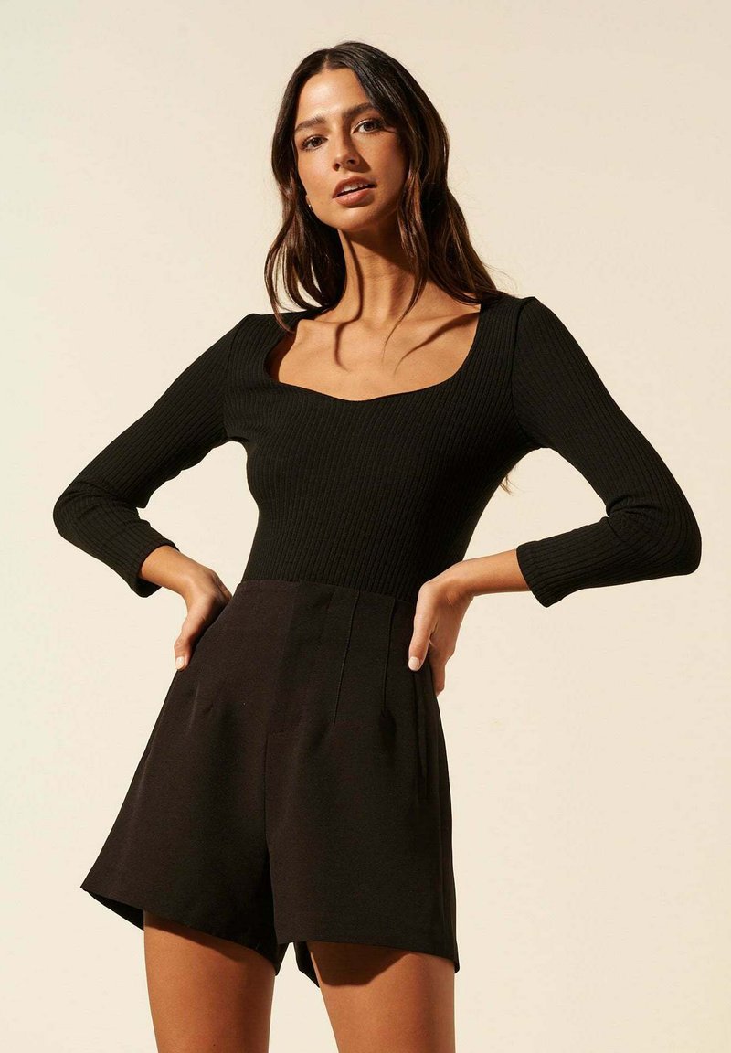 Bodysuit noir à côtes avec un décolleté carré, des manches longues et un short noir assorti avec des plis. Texture de tissu lisse.