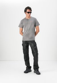 T-shirt de algodão cinza com um pequeno logotipo, combinado com calças cargo de couro pretas com bolsos e textura. Completo com ténis pretos.