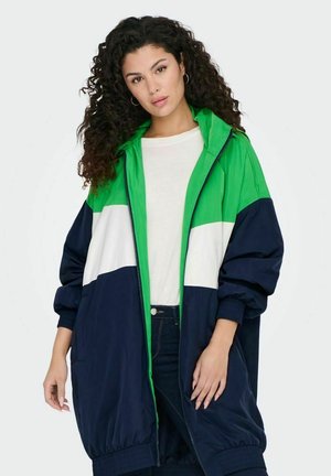 Color-blocked windbreaker in navy, white, and green. Features a zip front, hood, and elastic cuffs with a relaxed fit. Lightweight fabric.