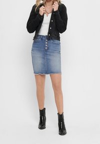 Jeanskjol med fem knapclosure, fransad fåll, ljusblå tvätt, i kombination med en åtsittande vit topp och svart jacka, svarta ankelstövlar.