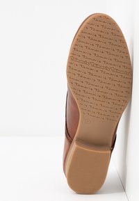 Chaussure en cuir brun avec un design de bout arrondi et lisse. Semelle en caoutchouc texturé beige avec un logo répété. Taille 37 indiquée sur la semelle.