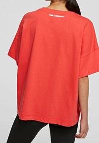 Løs pasform, kortærmet T-shirt i lys koralfarve lavet af blødt stof. Har en klassisk rund halsudskæring og logodetalje på ryggen.