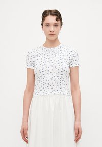 Wit T-shirt met korte mouwen en blauw bloemmotief, ronde halslijn, aansluitende body en een zachte textuur. Gecombineerd met een vloeiende witte rok.