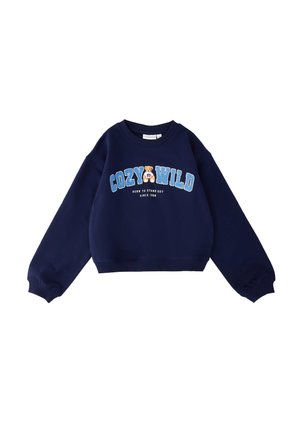 Sweat-shirt bleu marine à manches longues, avec "COZY WILD" inscrit en grandes lettres bleues, un graphisme d'ours en peluche et le texte "NÉ POUR SE DISTINGUER DEPUIS 1989" sur le devant.