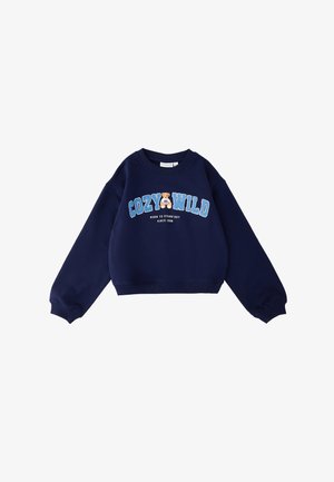 Sudadera azul marino de manga larga, con las letras grandes "COZY WILD" en azul, gráfico de osa de peluche y texto "NACIDO PARA DESTACAR DESDE 1989" en el frente.