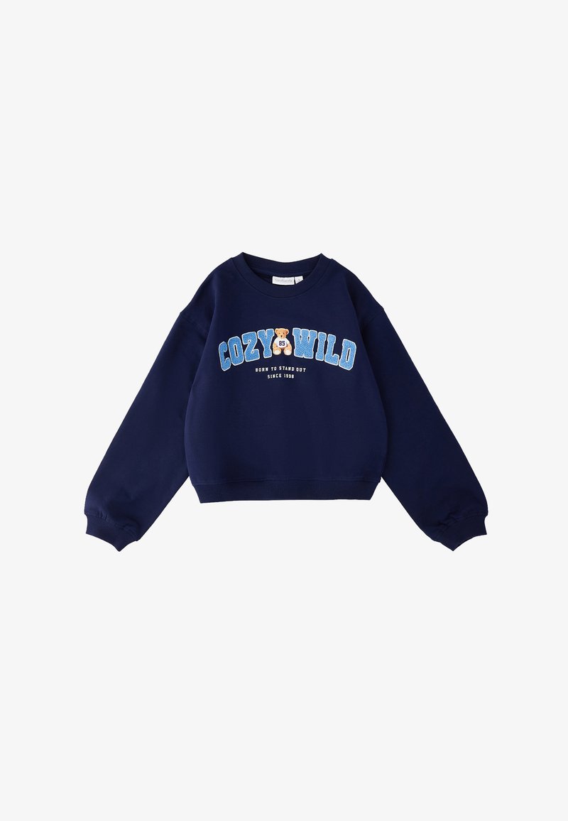 Sweat-shirt bleu marine à manches longues, avec "COZY WILD" inscrit en grandes lettres bleues, un graphisme d'ours en peluche et le texte "NÉ POUR SE DISTINGUER DEPUIS 1989" sur le devant.