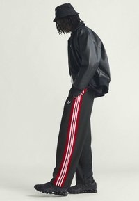 Svart oversized jacka, svart bucket hat, rödrandiga svarta sweatpants och svarta träningsskor, med en glänsande yta och rena linjer.