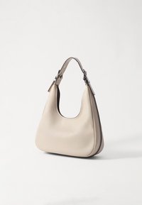 Sac à épaule en cuir beige avec une surface lisse et texturée, une forme incurvée et une seule bandoulière réglable avec des accents en métal argenté.