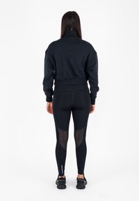 Zwarte sweatshirt met een hoge kraag, gecombineerd met zwarte legging met meshpanelen. Schoenen zijn zwarte hardloopschoenen. Eenvoudig, functioneel ontwerp.