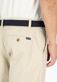 Beige cargo shorts with a woven navy belt, featuring a buttoned back pocket and a small "SEASIDE" label. Smooth, lightweight fabric.