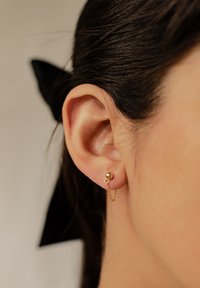 Goldohrstecker mit einer sphärischen Kuppel und einem kleinen Kettendetail. Sanfte Textur mit glänzendem Finish. Der Ohrstecker wird am Ohrläppchen getragen.
