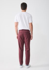 Burgundy trousers with a straight cut and belt loops, featuring two back pockets with button closures, paired with a plain white t-shirt.