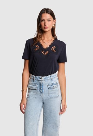 T-shirt blu navy con scollo a V decorativo e scollature a forma di cuore, completato da maniche corte, abbinato a jeans in denim chiaro a vita alta.