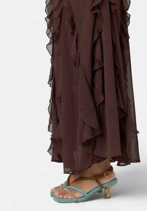 Falda marrón transparente con volantes, combinada con sandalias de punta abierta con tiras en verde azulado y beige y pequeños tacones dorados.