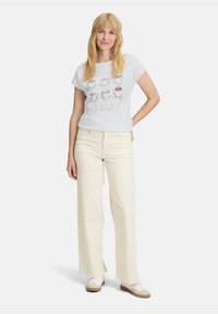 Hvid kortærmet t-shirt med illustrationer af kaffekopper og tekst, parret med højtaljede cremede wide-leg bukser og neutrale sneakers.