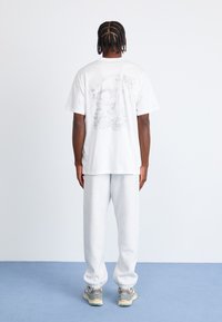 White cotton T-shirt with a detailed gray graphic on the back, paired with light gray sweatpants and multi-colored sneakers.