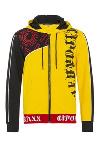 Gelb und schwarz gestreifter Zip-Hoodie mit Kapuze, grafischem Text in Schwarz und Rot, kontrastierenden Einsätzen und Seitentaschen; aus weichem Stoff.