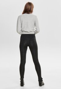 Svarta, glittriga leggings med en smal passform, tillverkade av stretchigt material, i kombination med en grå tröja. Leggingsen har en hög midja.