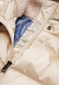 Lys beige pufferjakke, satin finish, med fuzzy lyserød foer. Har broderet "Bogner" på lynlåslappen og sølvfarvet hardware.