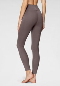 Leggings grigi con vita alta, texture liscia, design aderente e dettagli di cucitura lungo i lati.