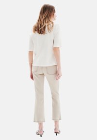 Beige ausgestellte Jeans und ein kurzärmliges cremefarbenes Oberteil. Das Outfit zeichnet sich durch eine glatte Textur und ein minimalistisches Design aus. Sanfte Farben mit subtilen Details.