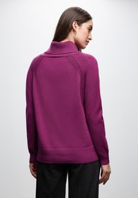 Fioletowy sweter z ściągaczem w kształcie turtlenecka; charakteryzuje się teksturowanymi akcentami na ramionach i luźnym krojem. Miękki materiał o gładkim wykończeniu.