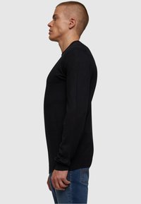 Schwarzes Langarmoberteil mit taillierter Passform, mit gerippten Bündchen und Rundhalsausschnitt, kombiniert mit blauen Jeans. Glatte Textur.