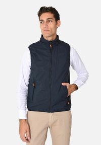 Gilet senza maniche blu navy realizzato in tessuto dalla texture liscia, con zip arancioni e due tasche laterali. Design con colletto alto.