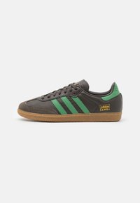Braune Ledersneaker mit grünen Streifen, Wildleder-Zehenkappe und Gummisohle. Branding an der Seite trägt die Aufschrift "adidas SAMBA."