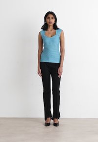 Top aderente turchese con dettagli testurizzati, abbinato a pantaloni neri su misura e tacchi neri eleganti. Design semplice, tessuto liscio.
