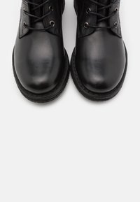 Bottes en cuir noir à bouts ronds, œillets métalliques et lacets. Les semelles en caoutchouc présentent un motif de grip texturé.