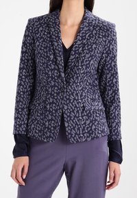 Námořnický blejzr s texturovaným vzorem leopardího tisku ve stříbrné barvě. Disponuje zapínáním na jeden knoflík a dvěma předními kapsami. Hladký povrch látky.