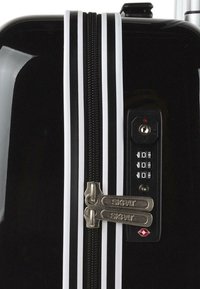 Maleta dura negra con dos cremalleras plateadas, acentos de rayas blancas, un candado de combinación y un acabado brillante y elegante.