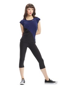 Canotta sportiva blu e nera con maniche corte, caratterizzata da un design a blocchi di colore diagonali. Abbinata a leggings neri alla caviglia e sneakers nere.