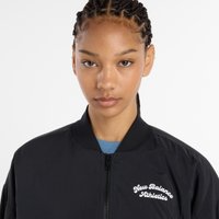 Casaco bomber preto com fecho à frente, colarinho em canelado e logótipo bordado "New Balance Athletics" no peito. Tecido leve, textura suave.