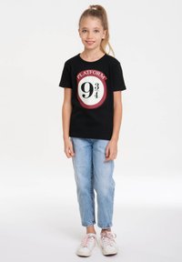 Black t-shirt with a round graphic featuring "PLATFORM 9¾" in white and red. Paired with light blue jeans and white sneakers.