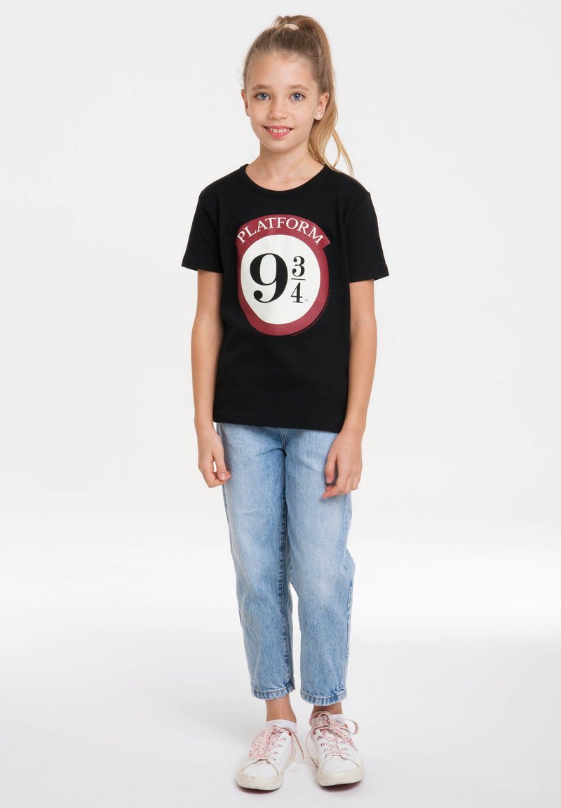 Black t-shirt with a round graphic featuring "PLATFORM 9¾" in white and red. Paired with light blue jeans and white sneakers.