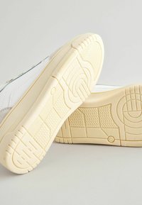 Schoenen met een bovenwerk van wit leer, grijze suède accenten en een beige rubberen buitenzool met een gestructureerd profiel voor grip.