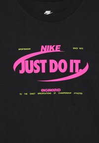 Juodas medvilninis marškinėliai su ryškiai rožine ir neonine geltona tekstu, įskaitant "NIKE" ir "JUST DO IT", su išlenktais dizaino elementais.