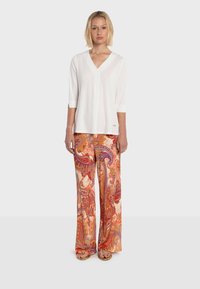 Blouse blanche à col en V avec manches trois-quarts, associée à un pantalon large à motifs éclatants aux teintes orange, rouge et violette.